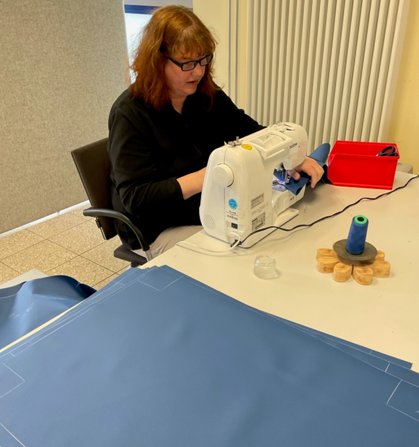 Frau führt Näharbeiten an blauem Stoff an einer Nähmaschine durch.