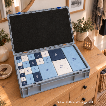 Geöffneter Portable Eurokoffer 2.0 auf einer hellen Holzkommode, bestückt mit 24 nummerierten Schachteln in verschiedenen Blautönen und Cremeweiß als Adventskalender.